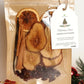 Packaged holiday potpourri with dried fruits and spices, featuring a tag on a neutral background.