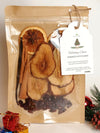 Packaged holiday potpourri with dried fruits and spices, featuring a tag on a neutral background.